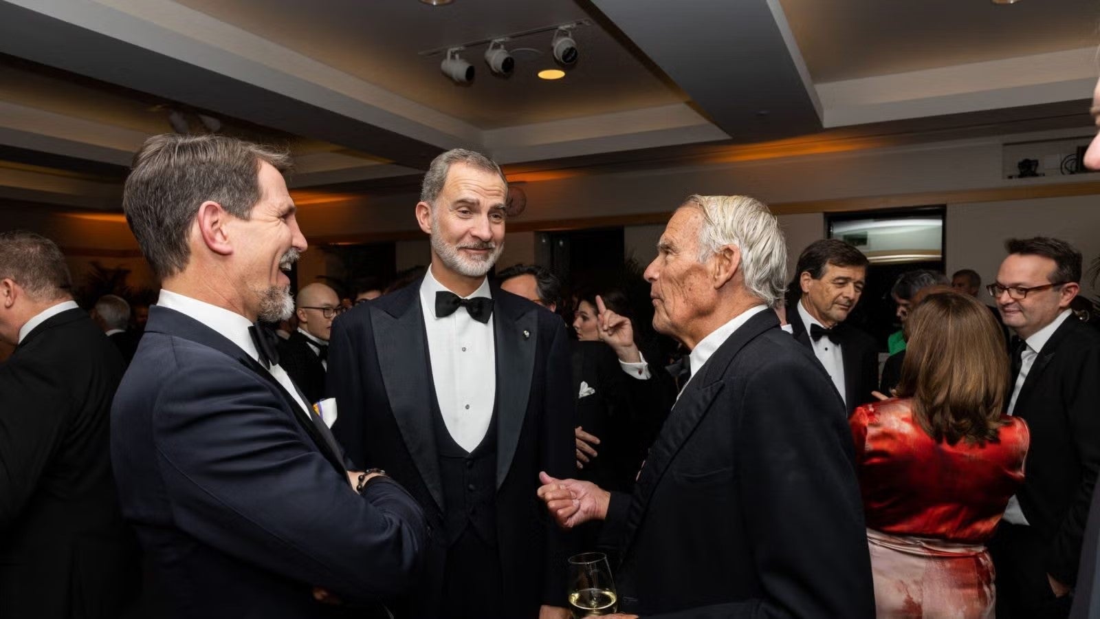 King Felipe of Spain in a black tuxedo, standing with two men at the gala, talking.
