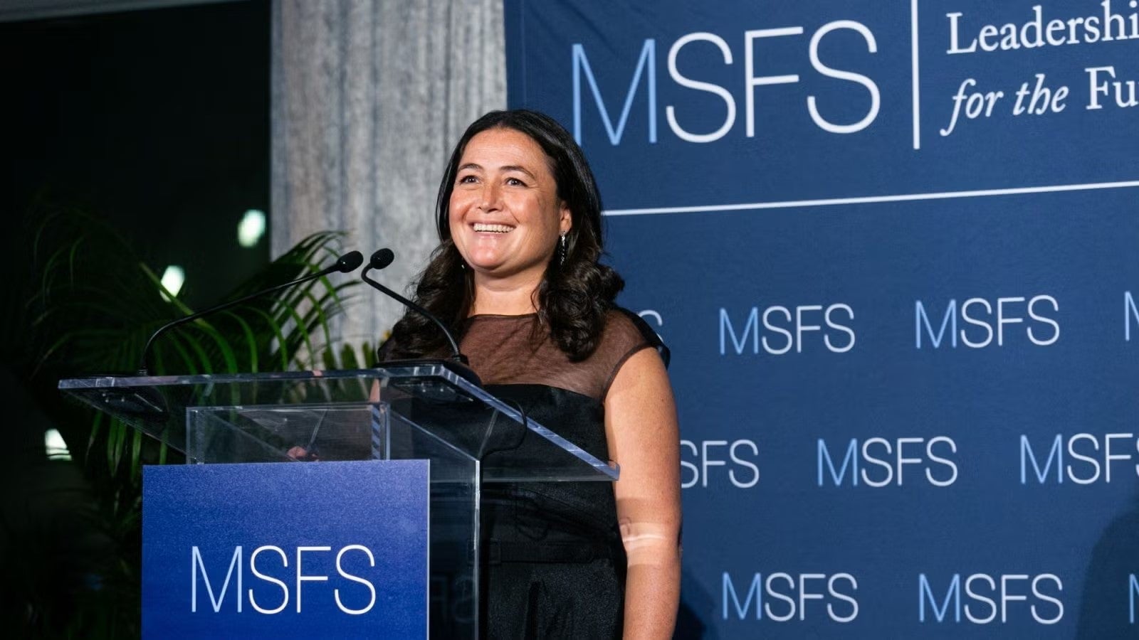 Ashley Lenihan in black dress standing at podium during gala.