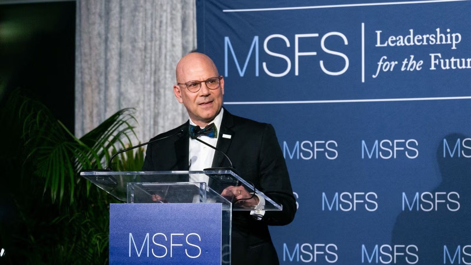 George Shambagh in tuxedo, standing at podium during gala.