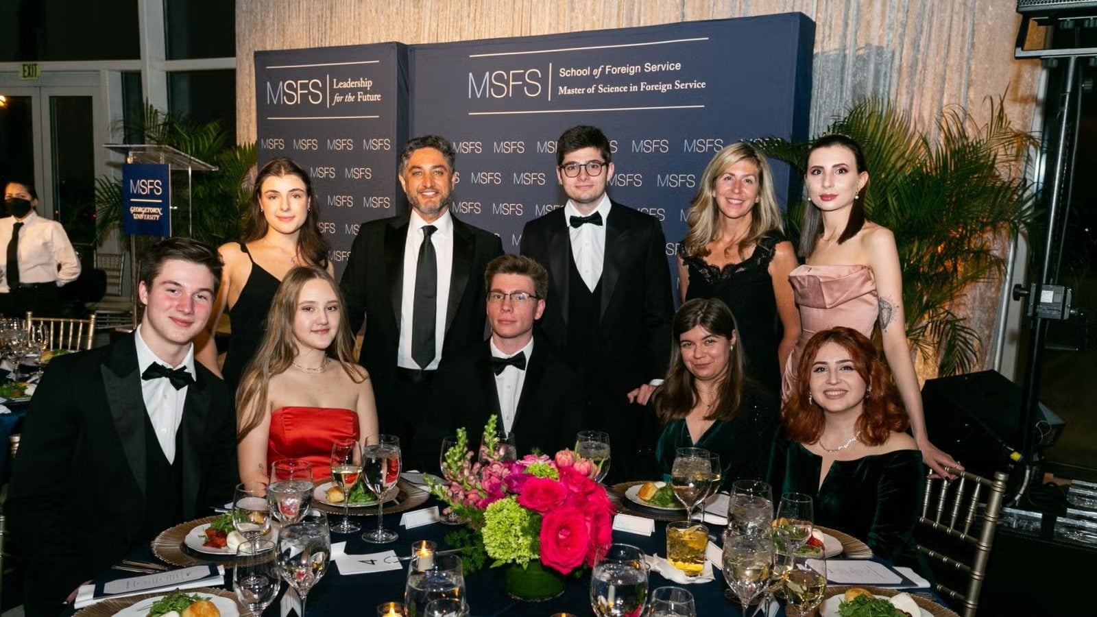 Ten SFS students in formalwear sitting and standing together around dinner table at gala.