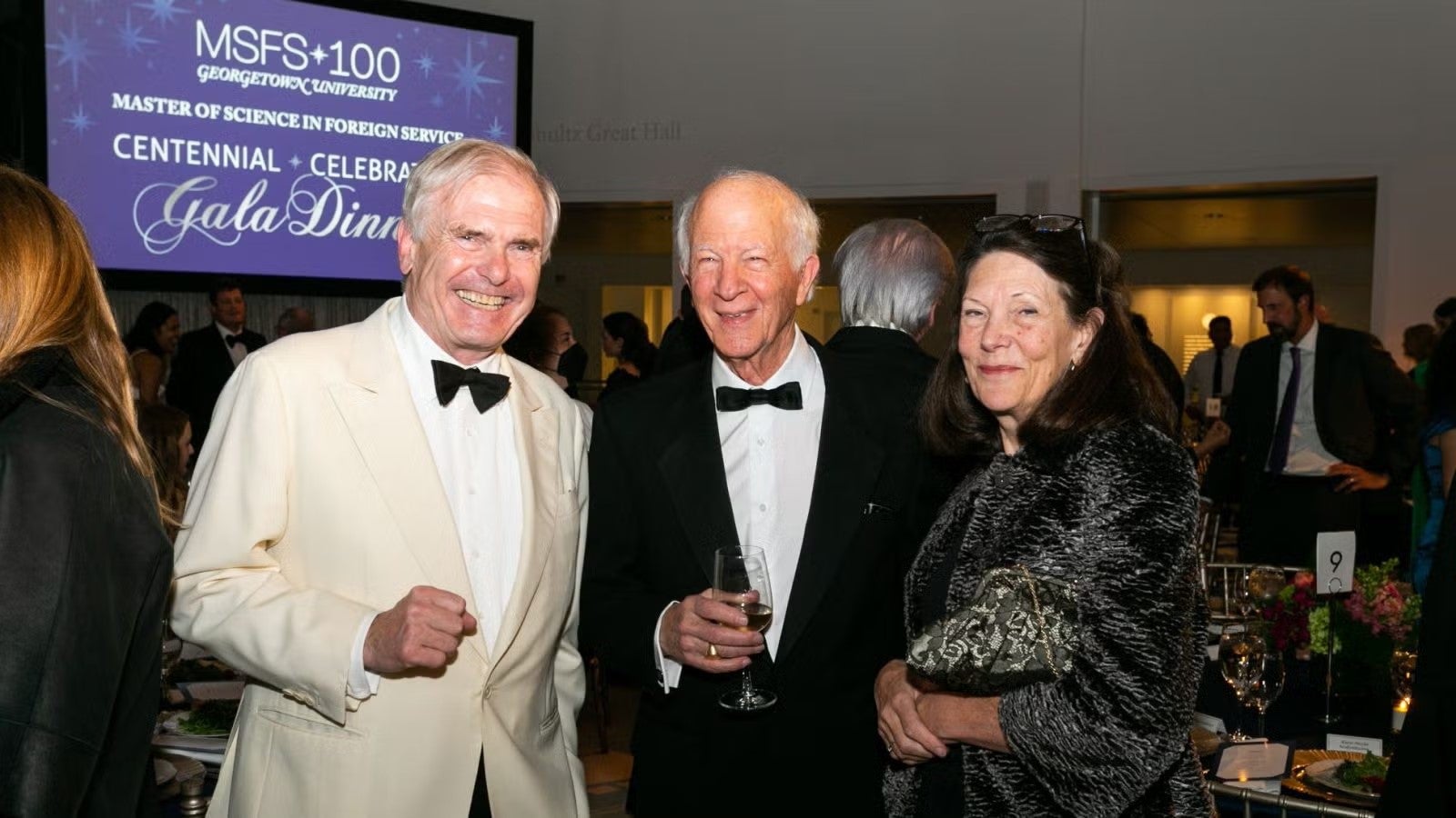 Two older men and one woman standing together, in formalwear, posing for photo at gala.
