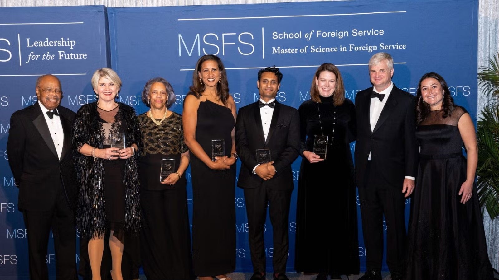 Men and women in dark formalwear standing together after just having received awards at gala.