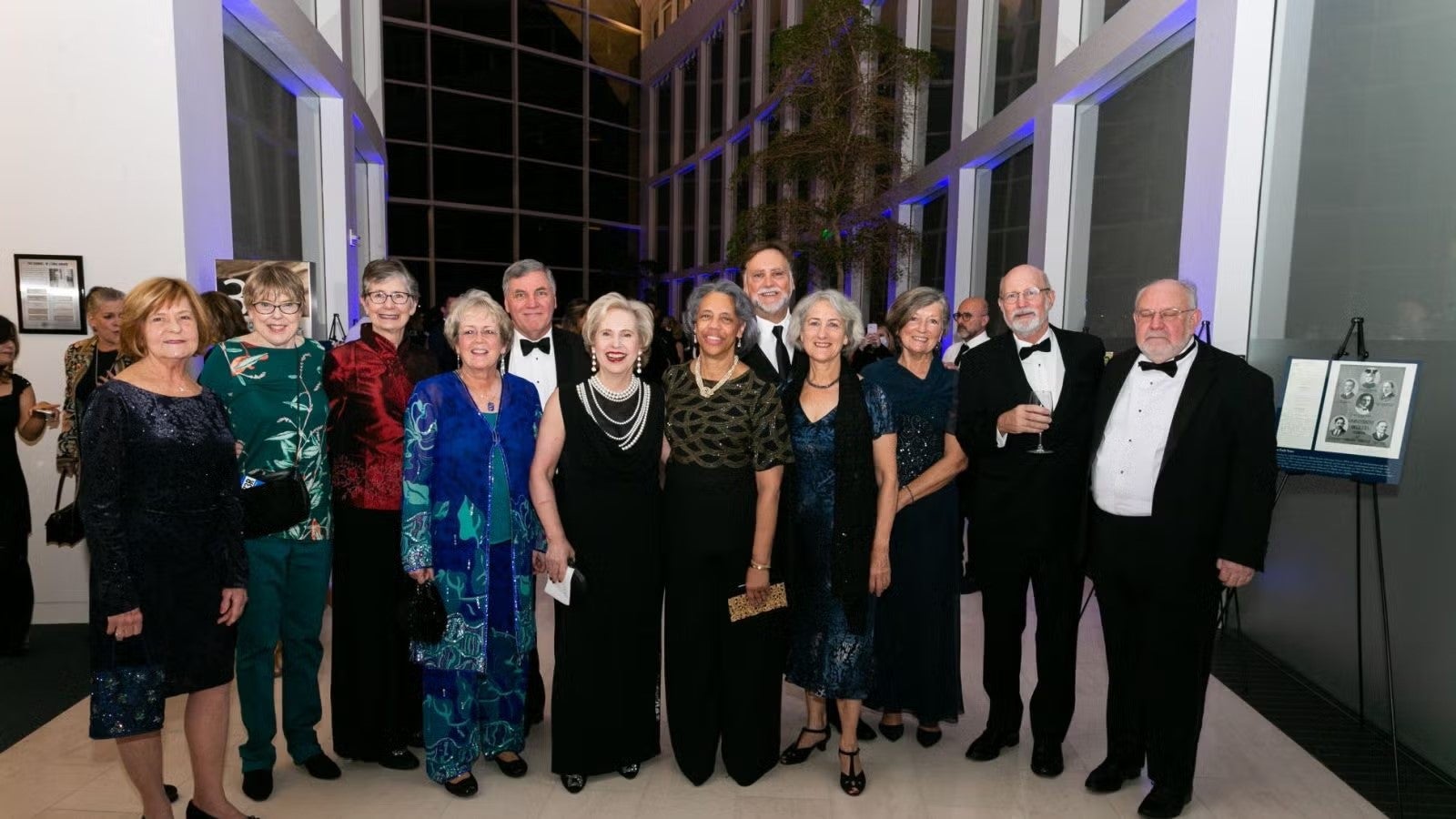 A large group of attendees at gala standing together for photo, in formalwear.