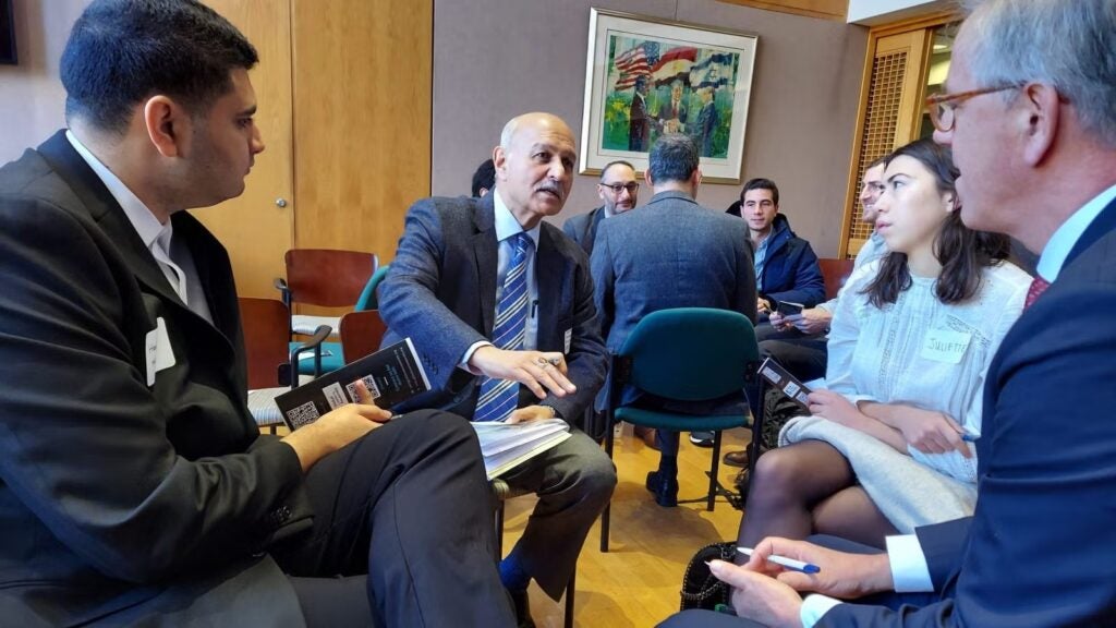 Four people in business attire sitting in circle having discussions in chairs.
