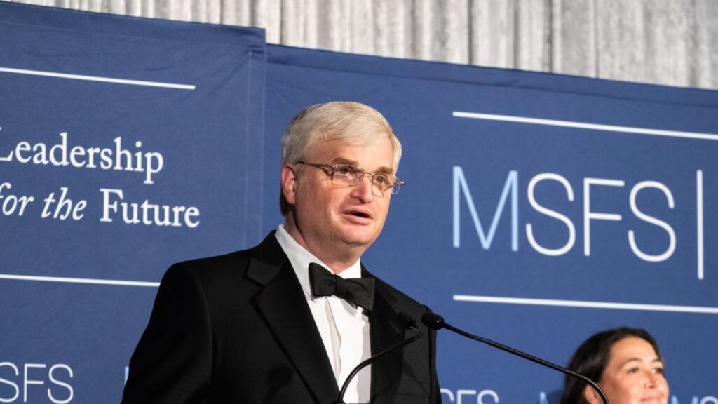 Man in black formalwear standing at podium during gala.
