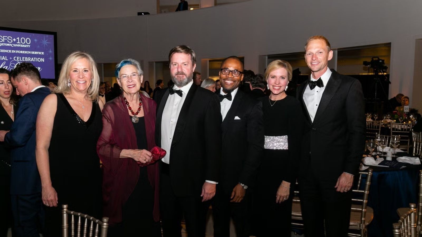 Small group of gala attendees standing together in formalwear.