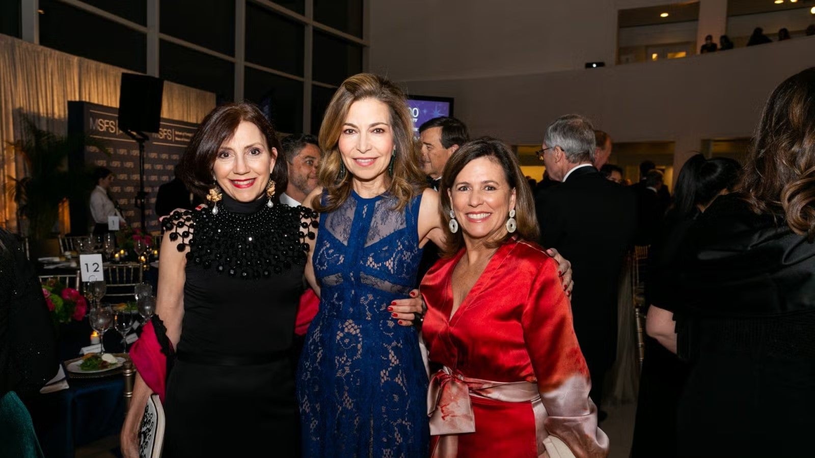 Three women in formalwear standing together for photo at gala.
