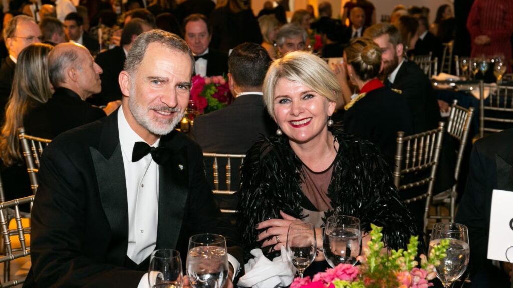 An older man and woman in dark formalwear sitting together at dinner during gala.