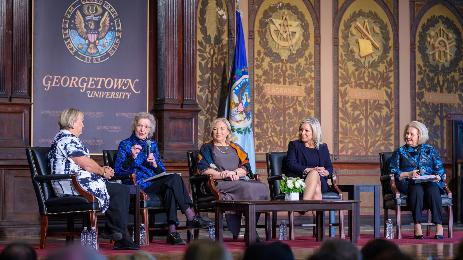 Wide shot of the stage in Gaston Hall, with speakers at the event conversing