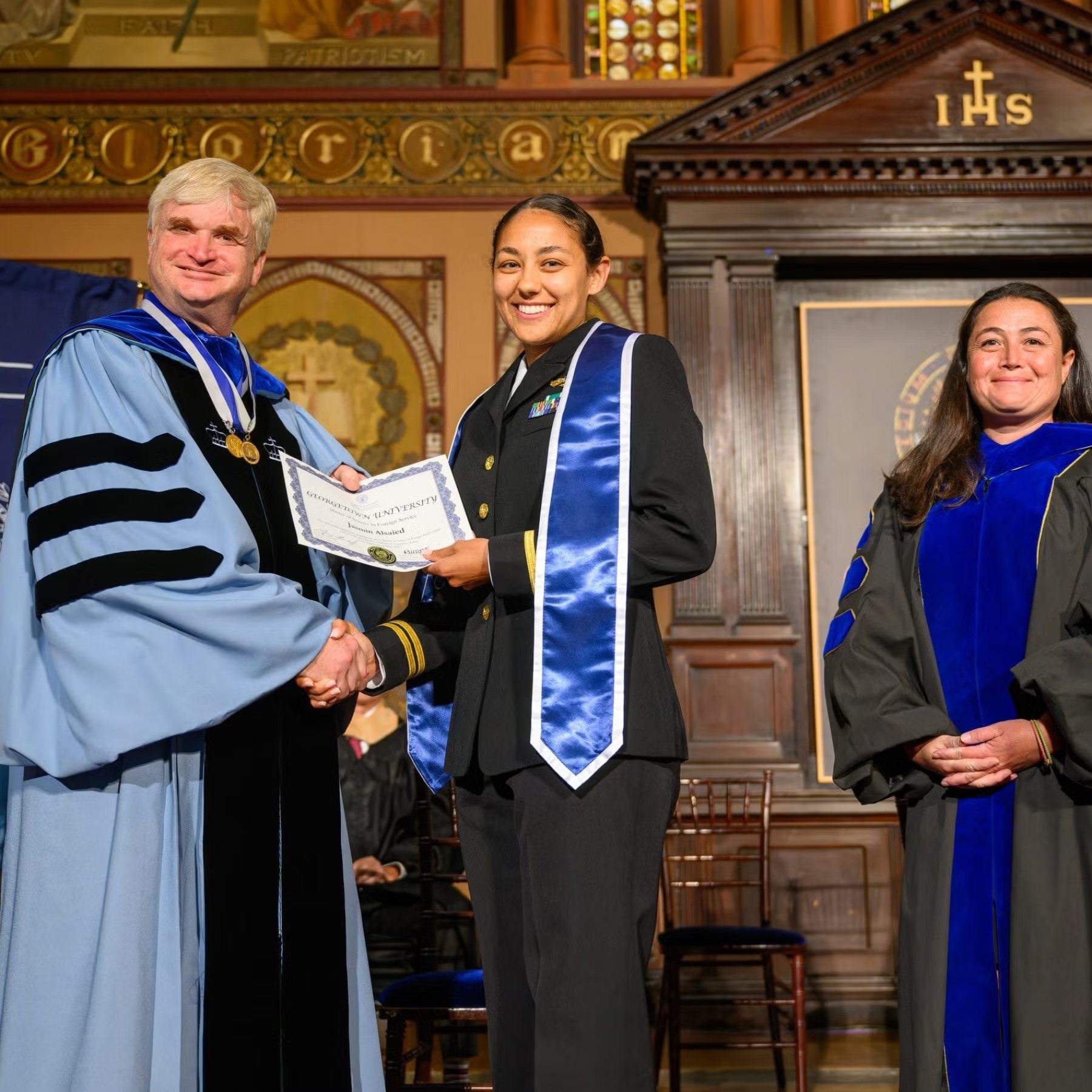 Jasmin Alsaied at commencement receiving MSFS diploma, shaking hands with SFS administrator wearing full doctoral regalia.