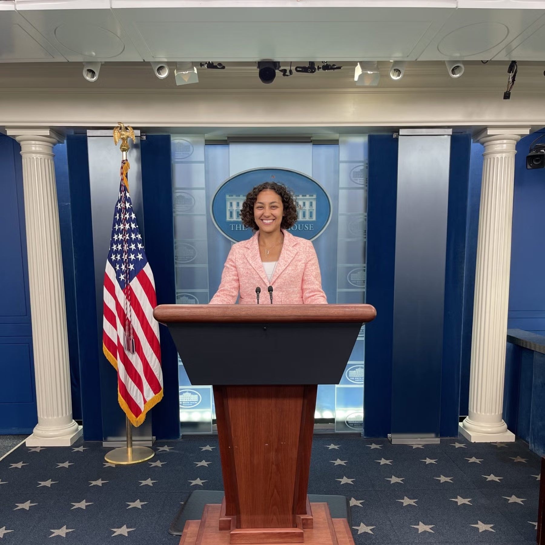 Jasmin Alsaied standing in light pink suit at White House podium.