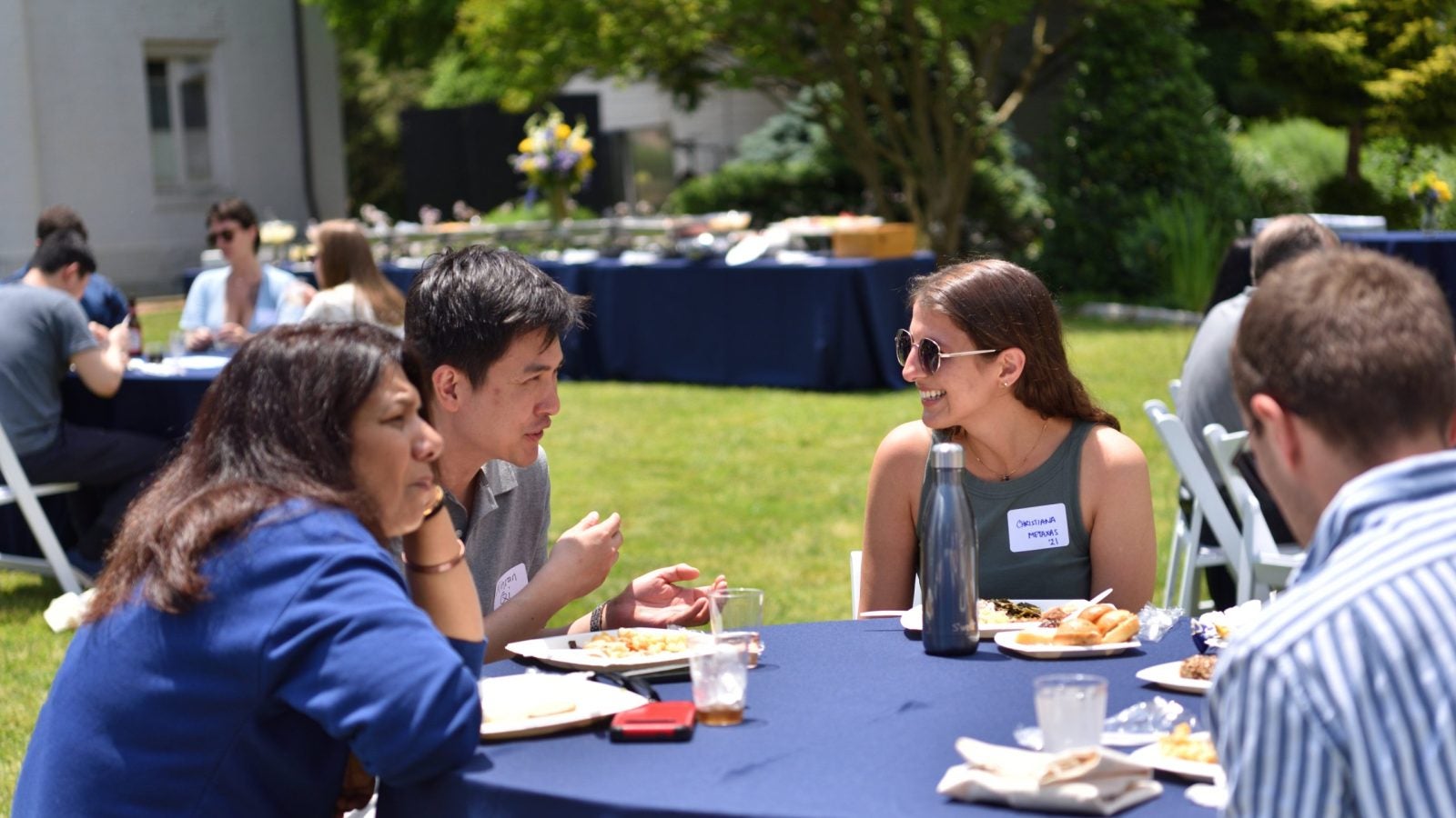 A group of people sitting at a table outside talking and smiling