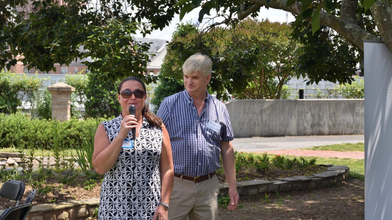 Two people standing together outside. One is speaking into a microphone.