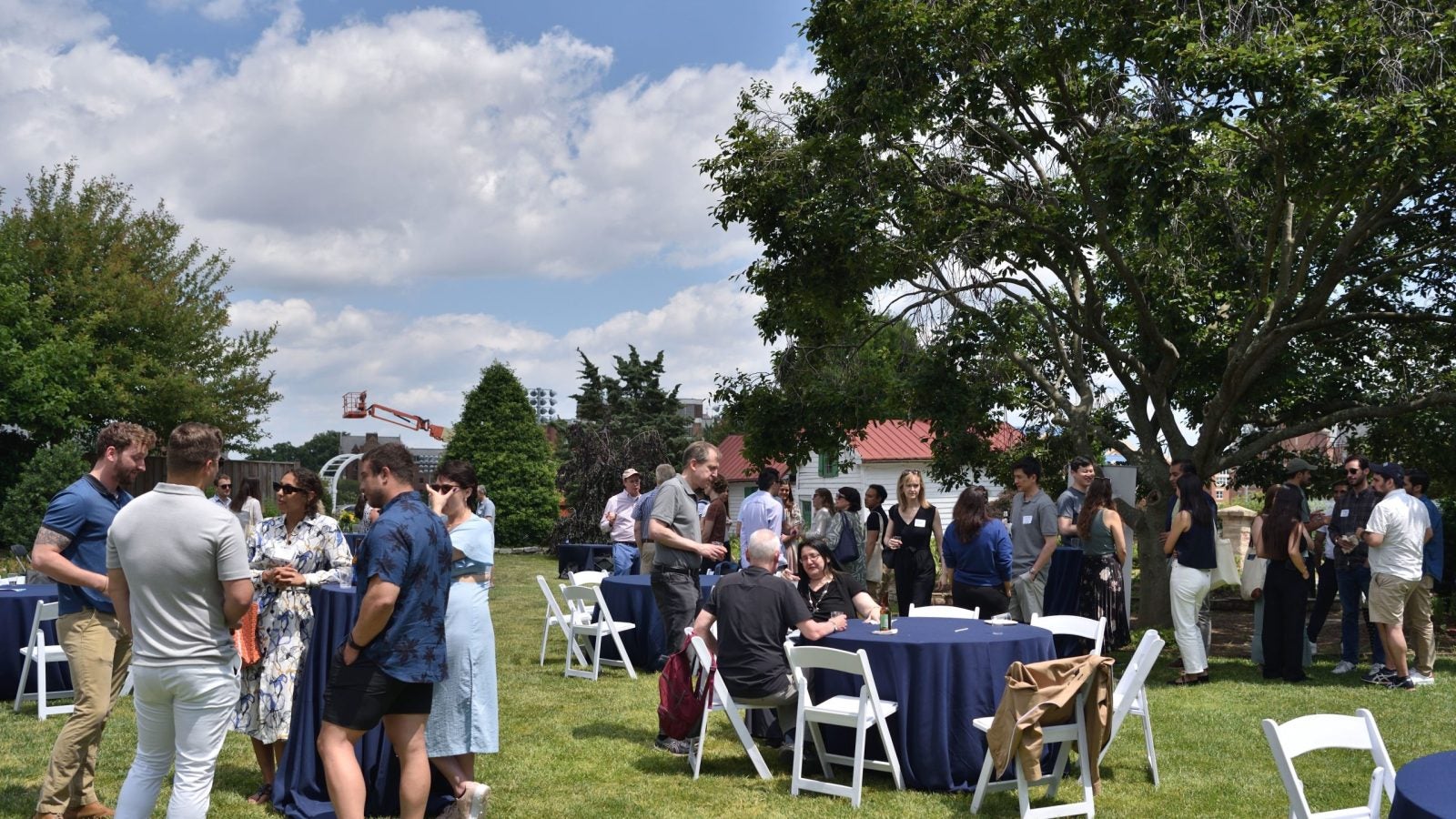 A large group of people standing and sitting at tables and talking during an outdoor reception.
