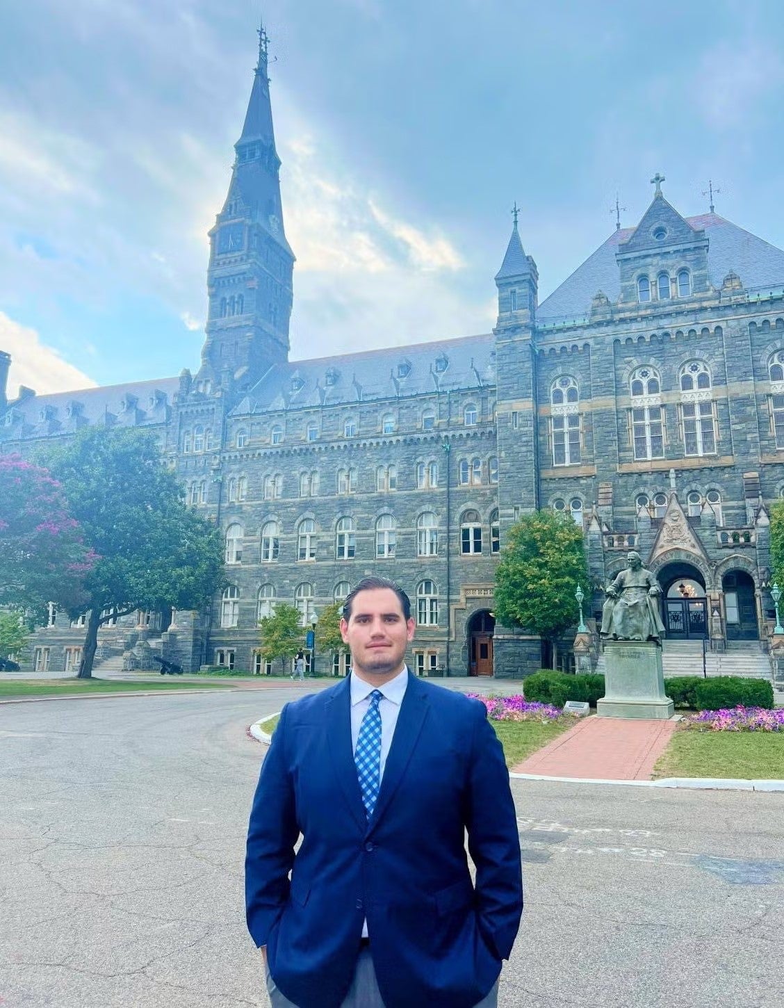 Abe Ahmad standing in front of Healy Hall in a navy blue suit, white shirt, and light blue tie.