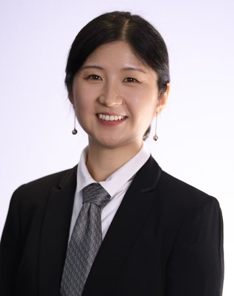 In-Hwan "Helen" Heo headshot. She is wearing a black blazer, white shirt, and dark gray tie.