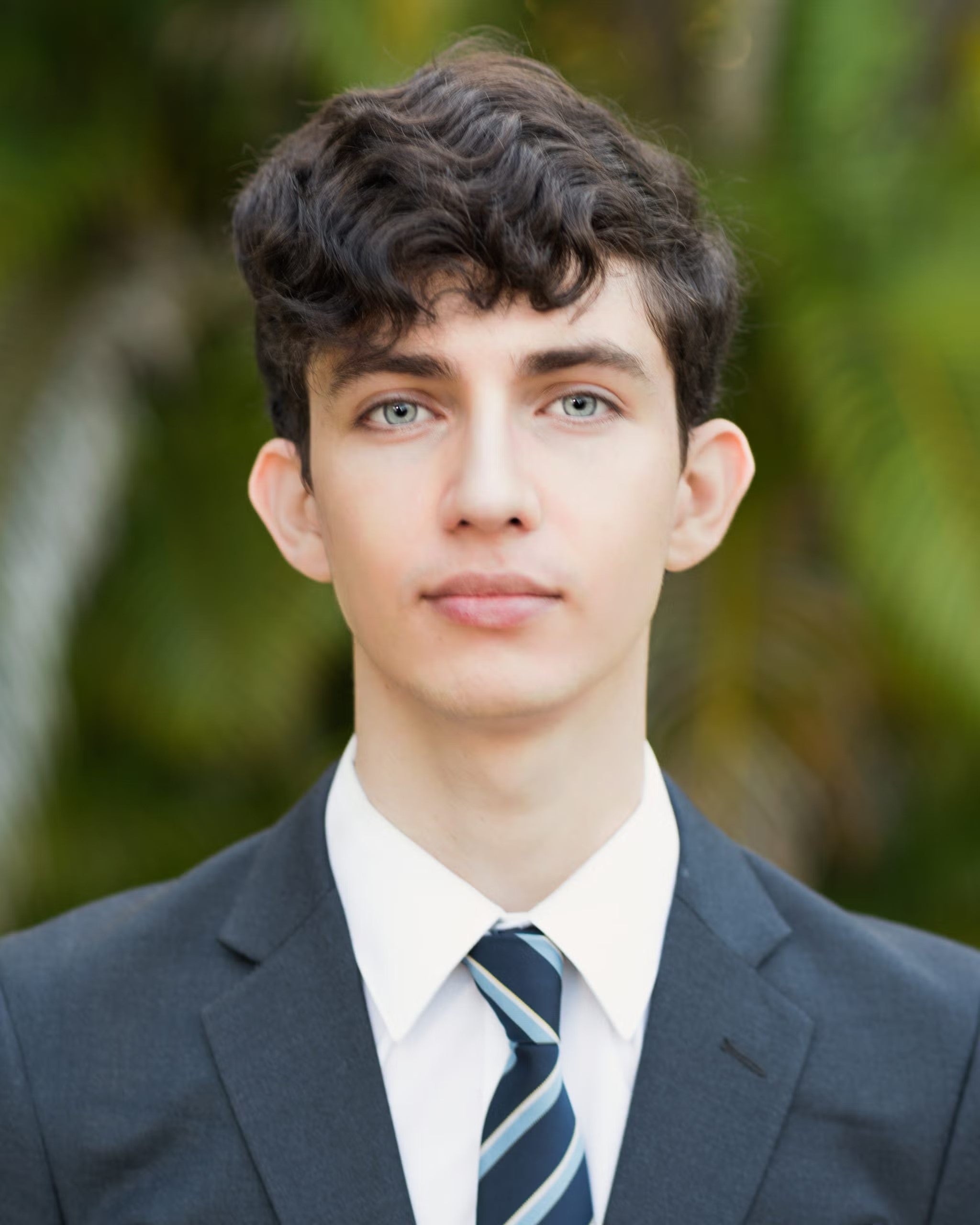 Maximo Ulloa Headshot. He is wearing a navy blue blazer, white shirt, and navy blue and light blue-striped tie.