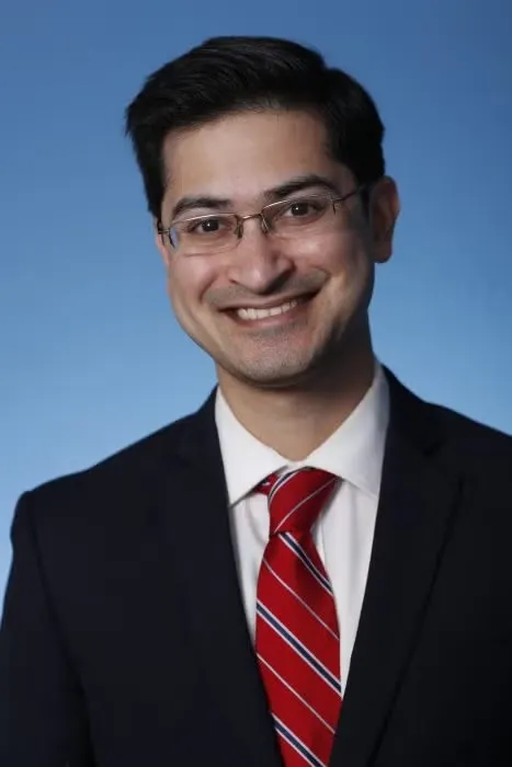 Headshot of Rush Doshi, wearing black blazer, white shirt, and red tie.