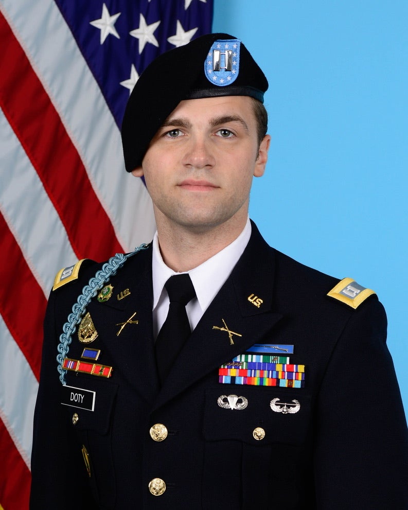 U.S. Army officer in dress uniform standing in front of the American flag.