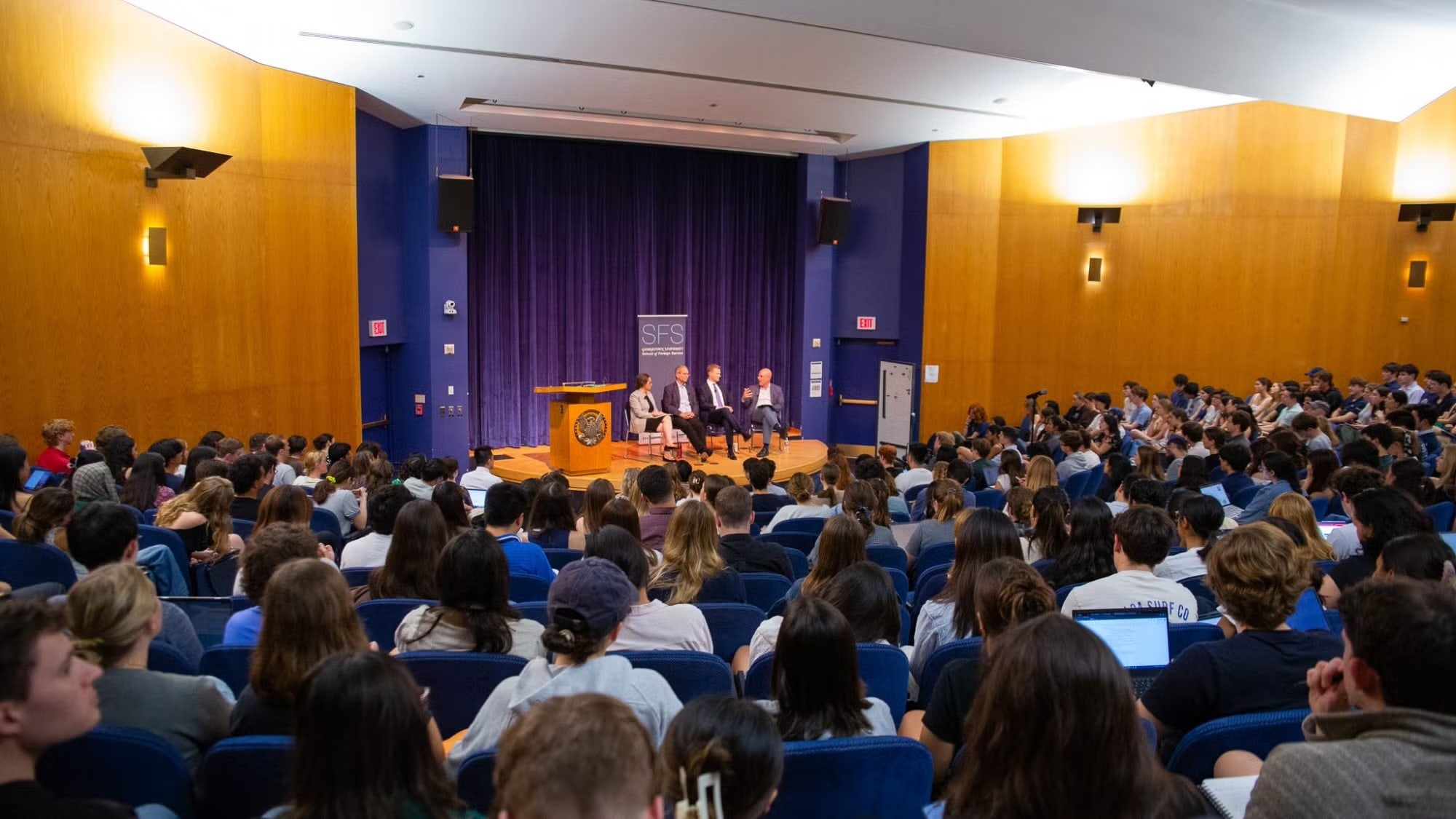 Event at Georgetown University's School of Foreign Service, featuring four speakers on stage in front of an audience of students in a packed auditorium.