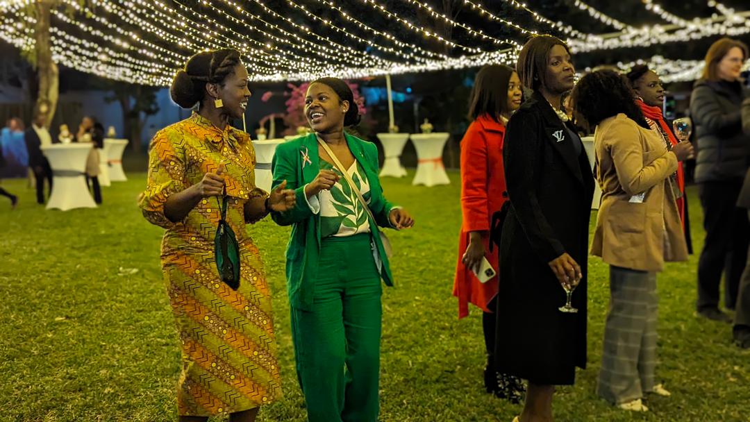 Two individuals interact at an outdoor evening event under strings of lights. The attendees are dressed in formal attire.