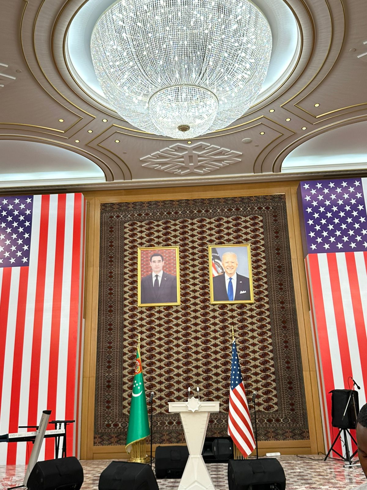An ornate conference room featuring two large United States flags flanking a podium.
