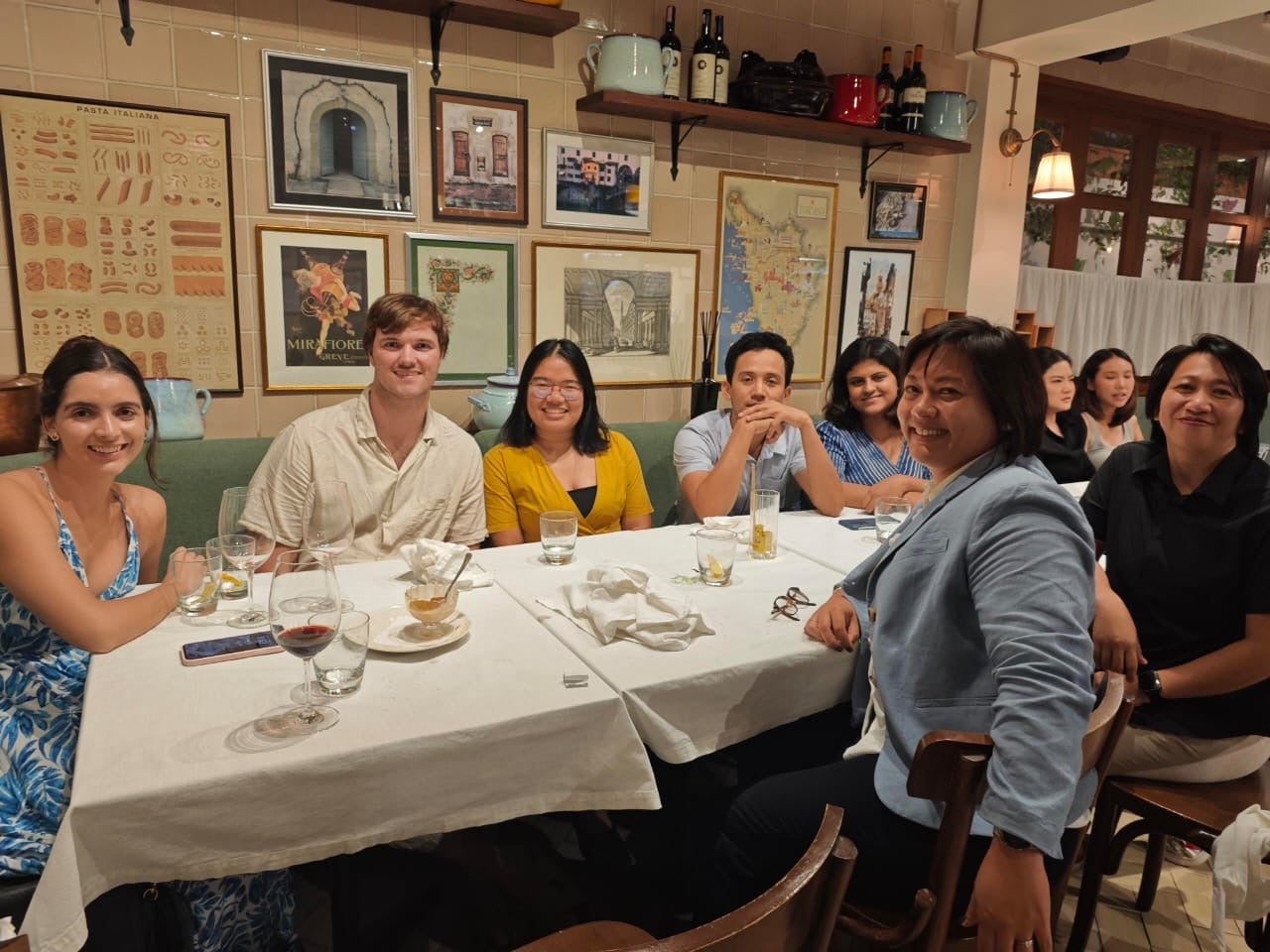 Group of people enjoying a meal around a table in a restaurant with wine glasses and menus visible.