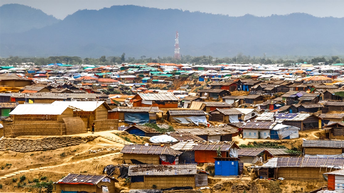 Panoramic view of refugee camp in Bangladesh with dense clusters of makeshift shelters spread across a hilly terrain.