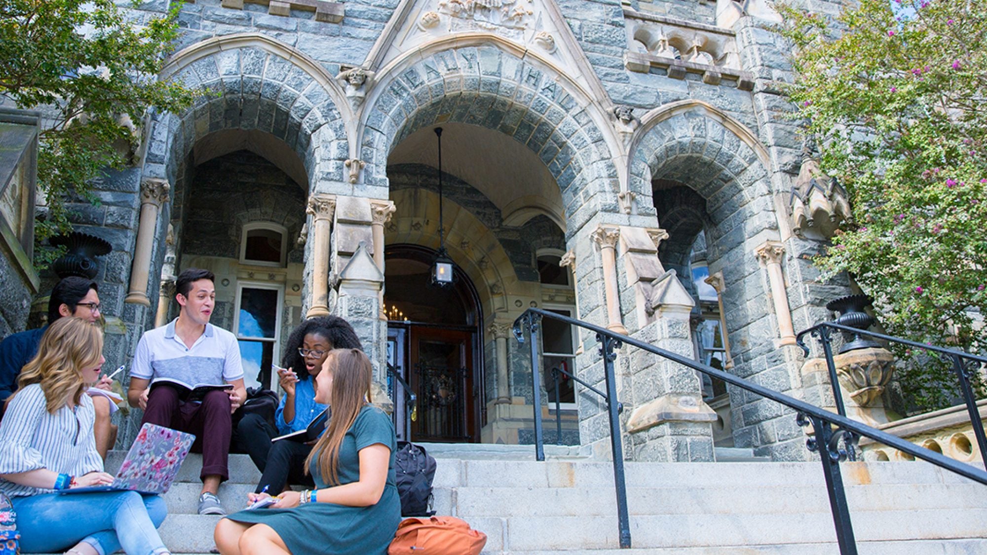 A group of students sit on the steps of Healy Hall