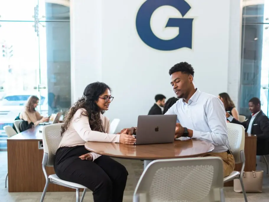 Two students at a table, looking at a laptop together.