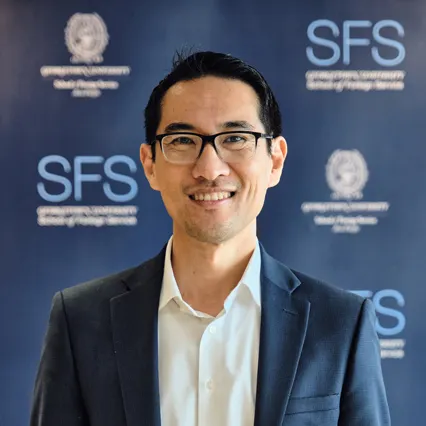 Headshot of Yuhki Tajima smiling in front of Georgetown SFS Asia Pacific backdrop