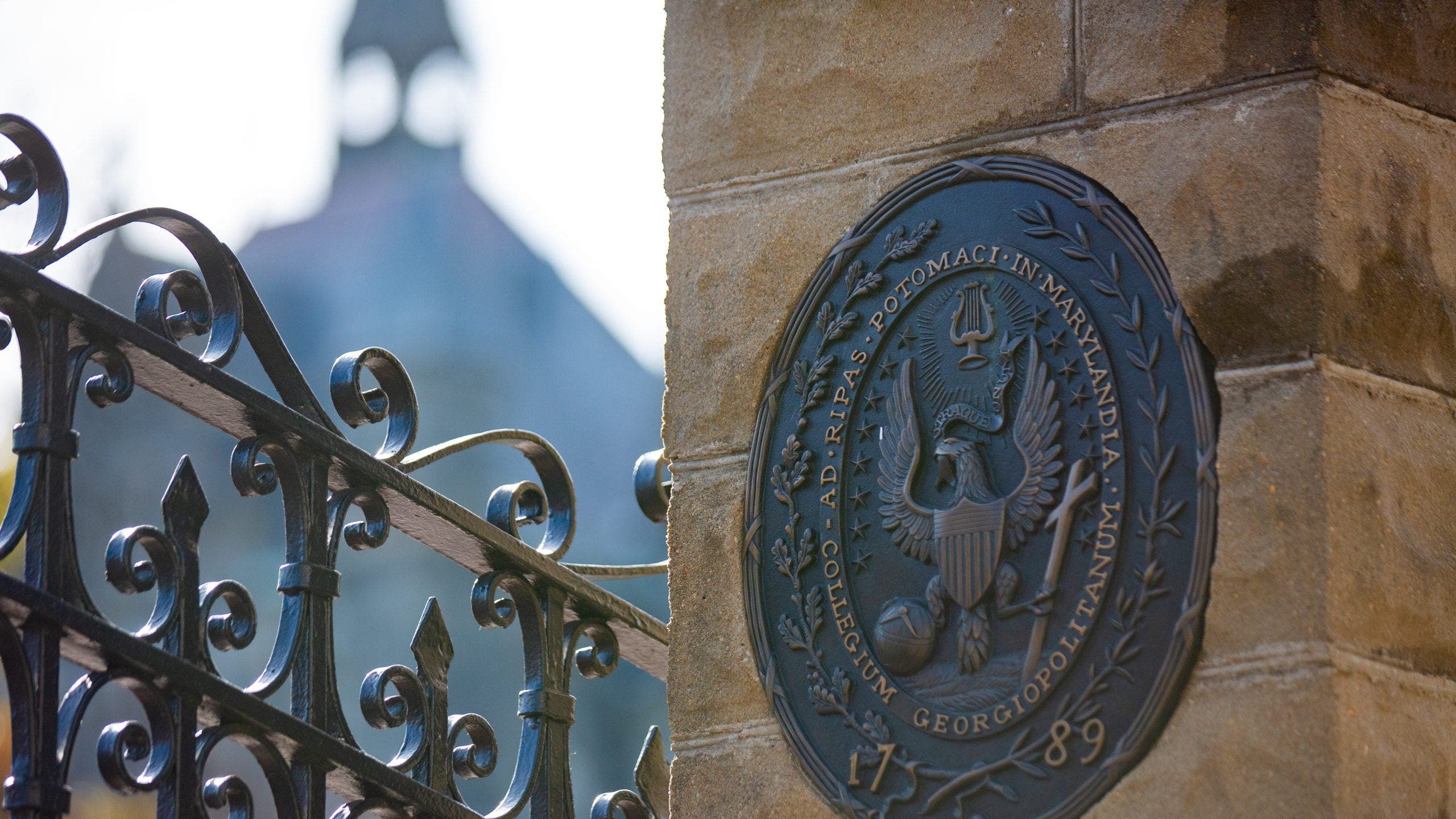 Outside gate of Georgetown University and university seal on a stone wall.