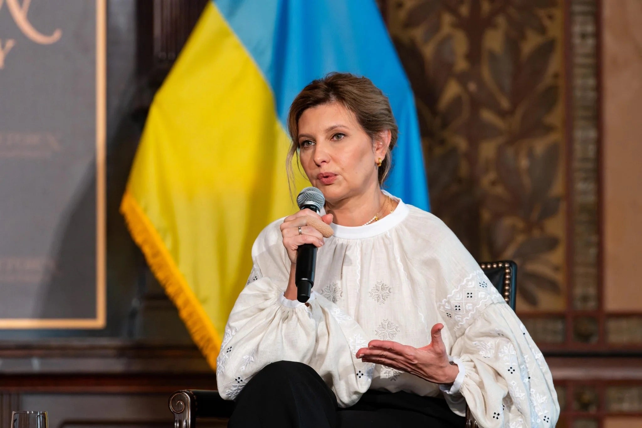 The First Lady of Ukraine, Olena Zelenska, seated in front of a Ukrainian flag.