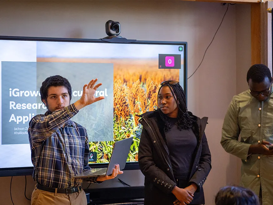Students giving a presentation, behind them a screen with a slide