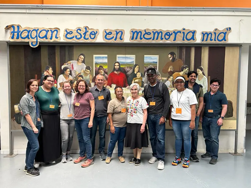 A group of students and professors. Behind them a reinterpretation of the Last Supper, with the words "Hagan esto en memoria mía"