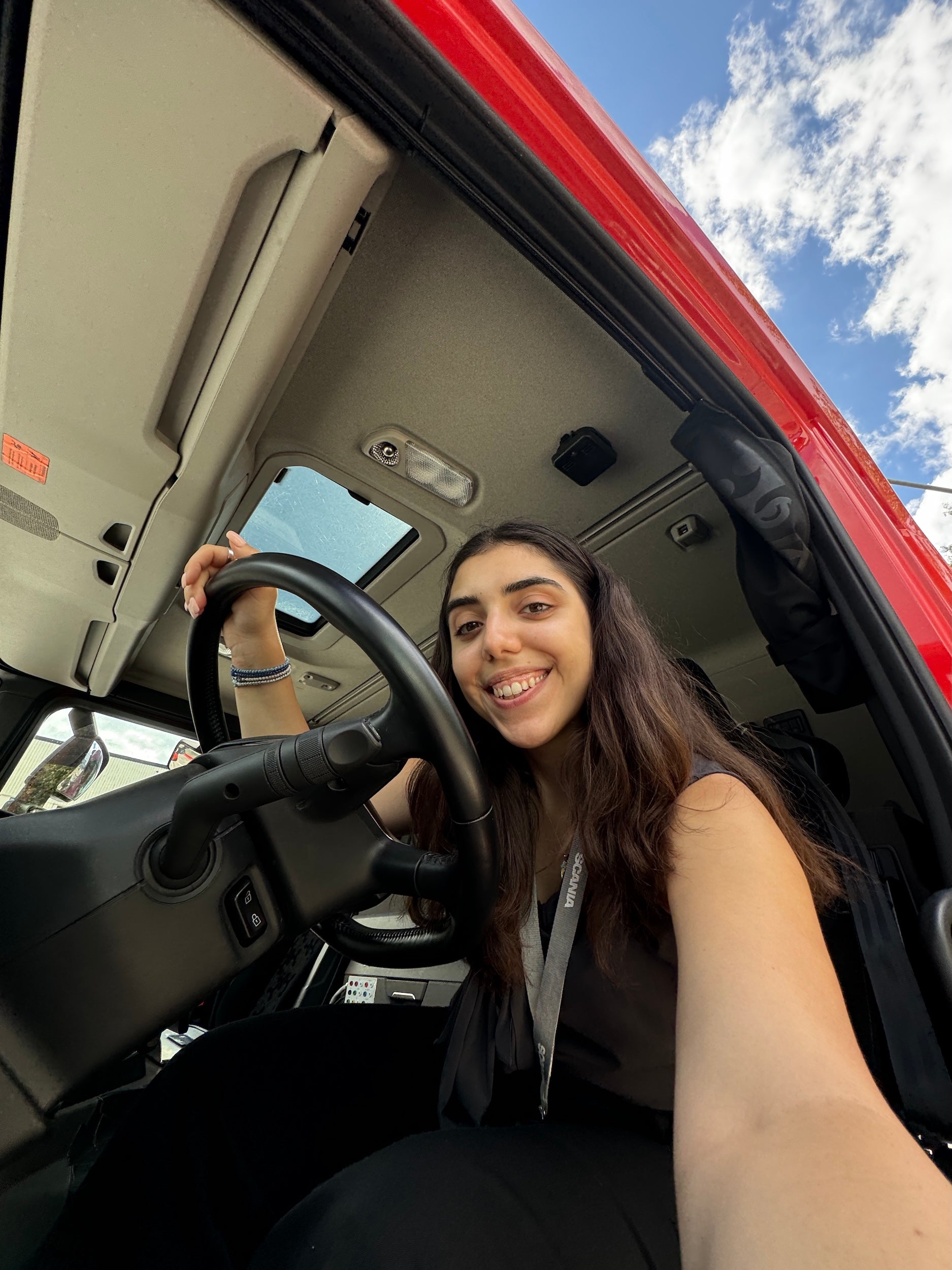 Person smiling while sitting in the driver's seat of a red vehicle, holding the steering wheel.