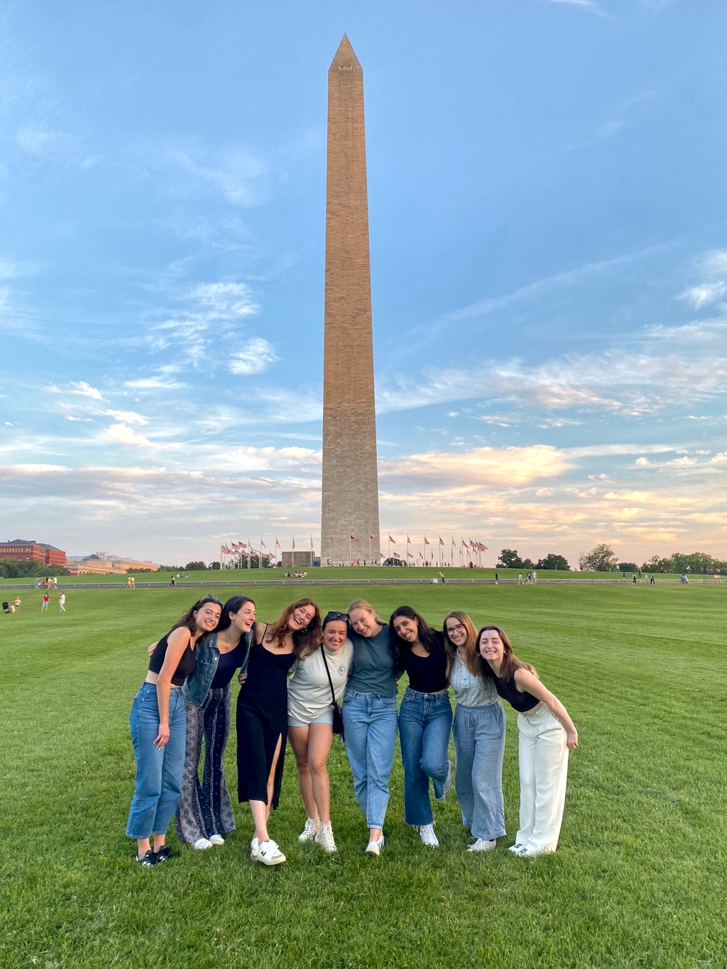 Group of seven individuals posing happily in front of the Washington Monument at dusk.