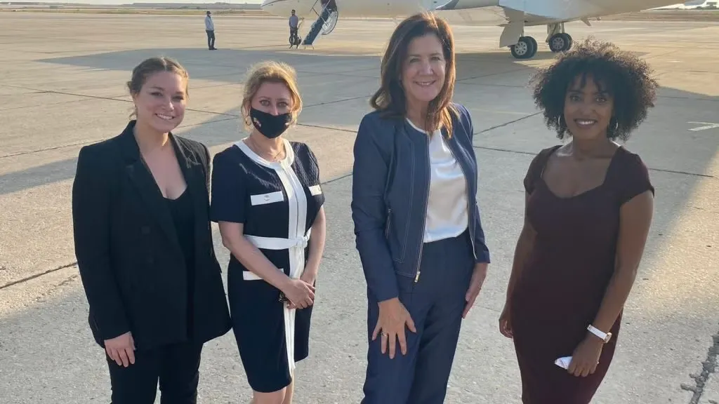 Photo of Yifter (right), Amb. Shea (second-to-right) and two other people, all in professional clothes, smiling on an airport runway with a plane behind them.