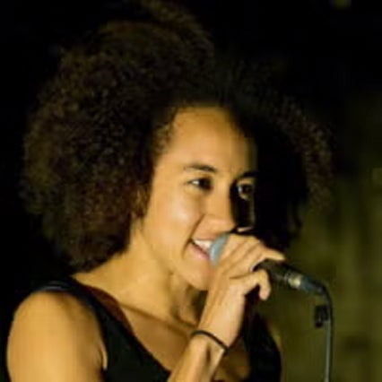 Headshot of Corina Kwami singing, holding a microphone close to her mouth