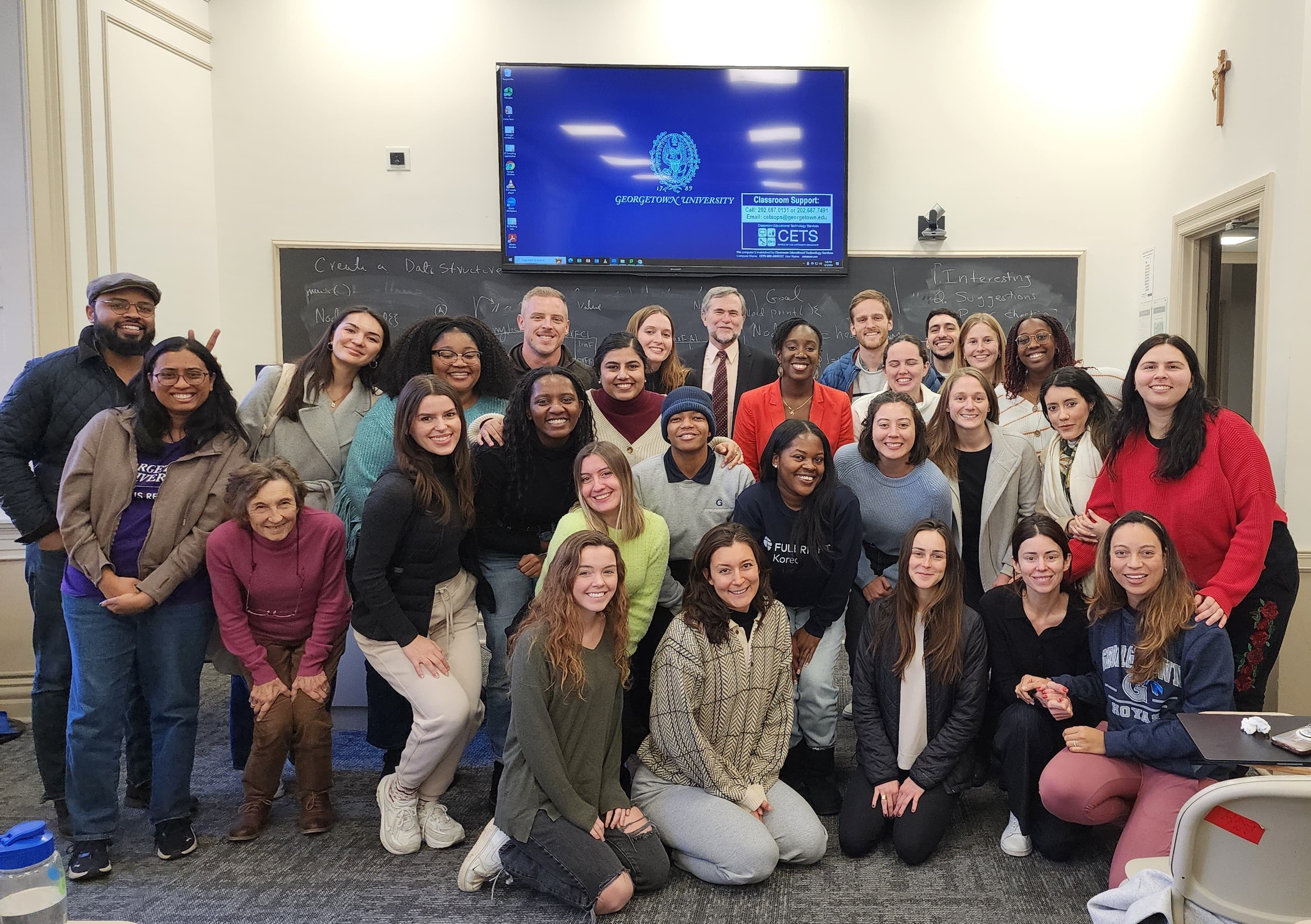 A group of people smiling for a photo in a room with a digital screen in the background.