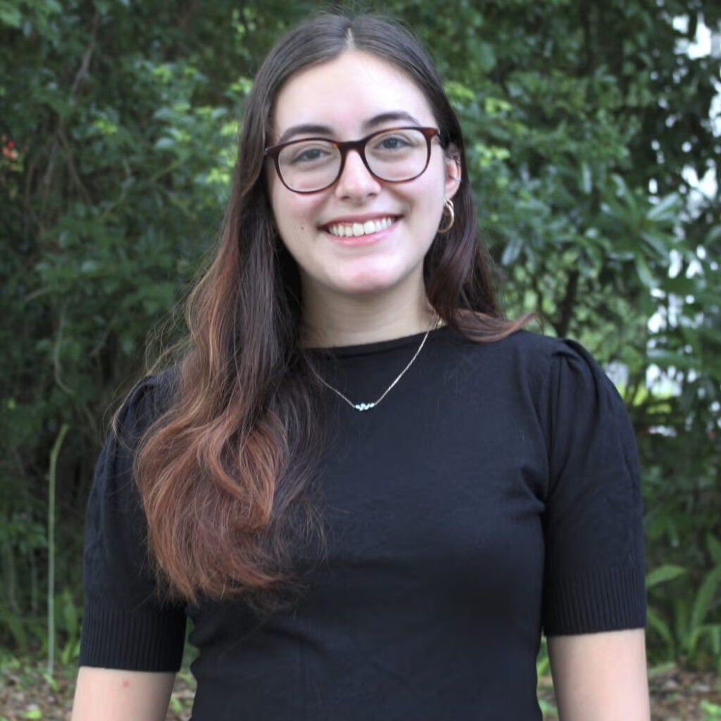 Emily Benedicto wearing a dark blouse and glasses, smiling.