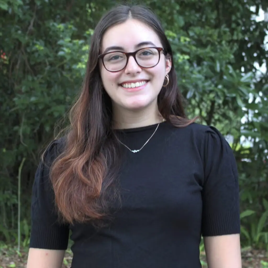 Emily Benedicto wearing a dark blouse and glasses, smiling.