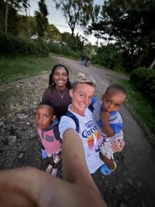 Group of people, including children, smiling and posing for a selfie on a tree-lined dirt road at dusk.