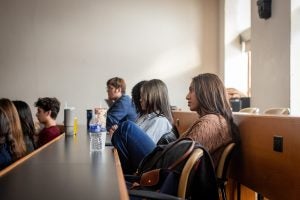 Students seated at desks attentively listening to a lecture in a classroom.
