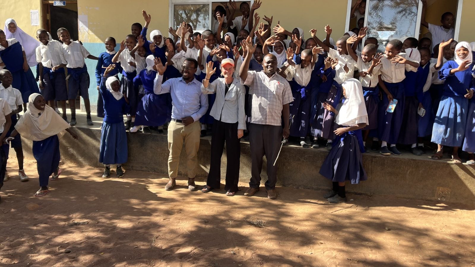 Group of students and teachers waving and celebrating in front of a school building.