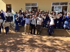 Group of students and teachers waving and celebrating in front of a school building.