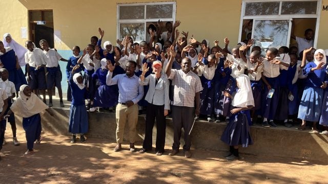 Group of students and teachers waving and celebrating in front of a school building.