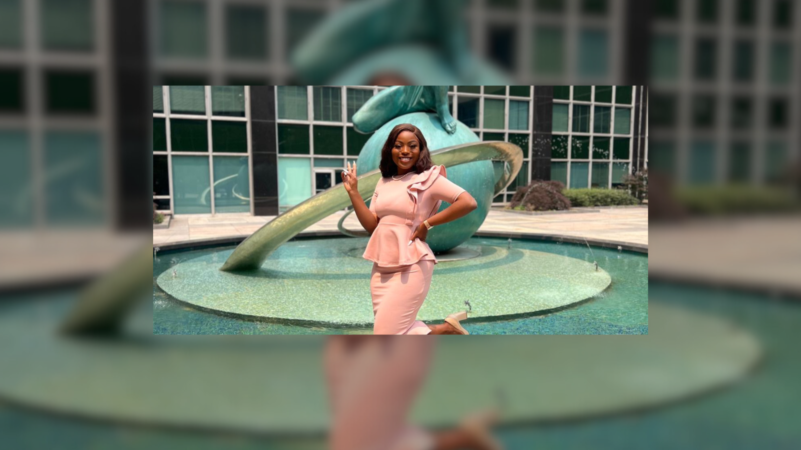 Person posing with hands on hips in front of the United Nations sculpture, smiling at the camera.