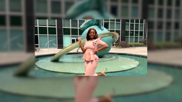 Person posing with hands on hips in front of the United Nations sculpture, smiling at the camera.