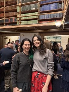 Two individuals posing for a photo in a room with elegant décor in the background.